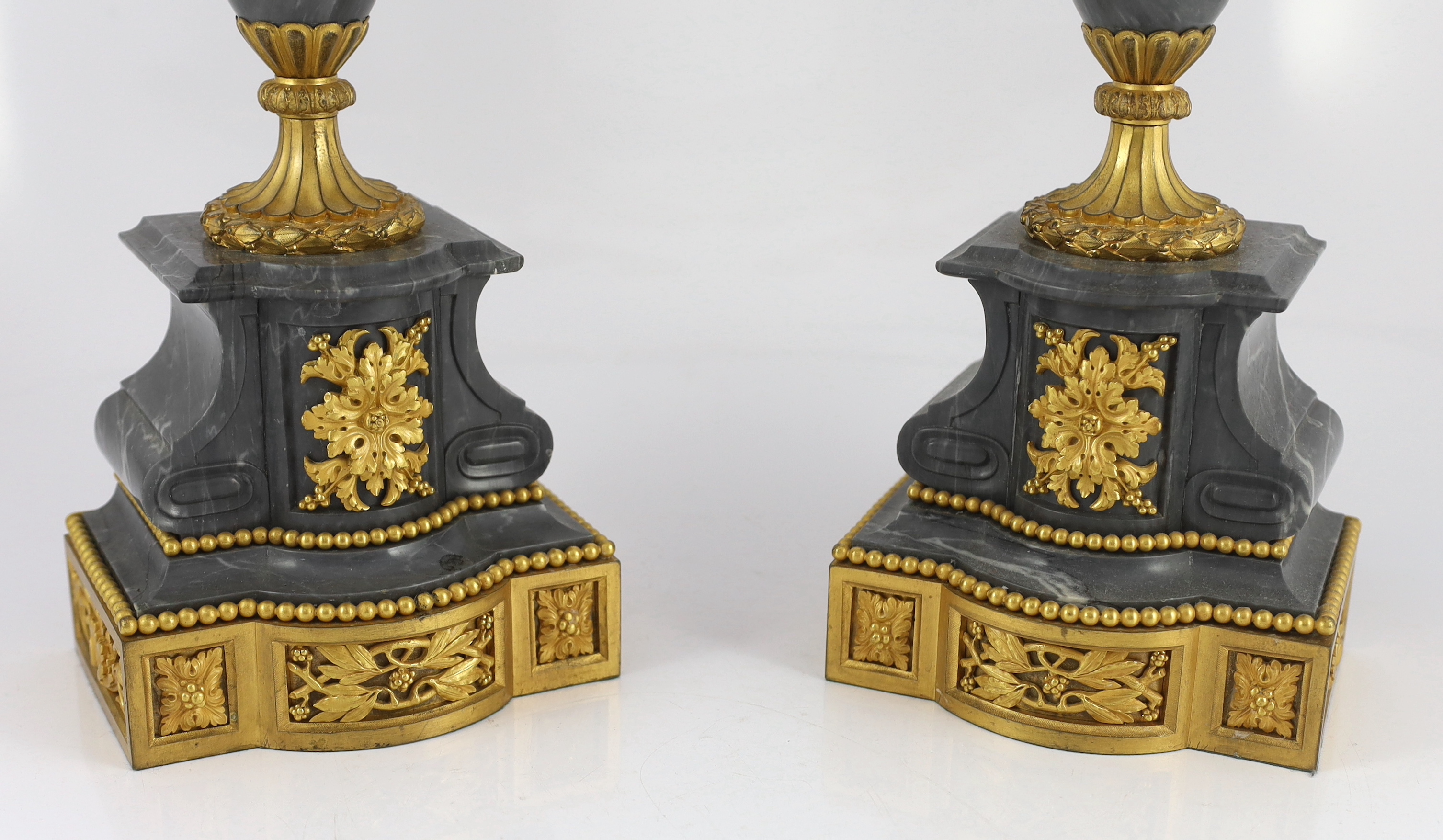 A pair of Louis XVI style ormolu and grey marble five light candelabra, with scrolling branches and urn shaped stems on architectural plinths, 26cm wide, 63cm high
